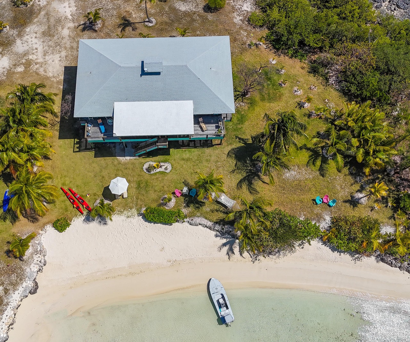 Top-down drone view of the property: the villa's roof, the garden with kayaks, and the crescent of secluded beach