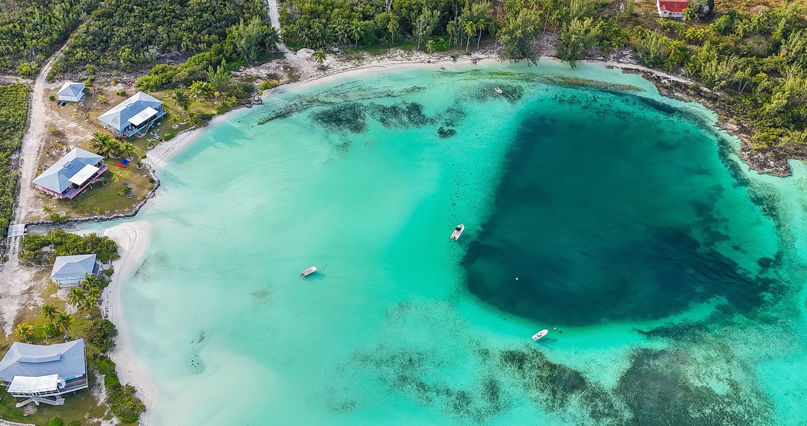 Aerial view of the blue hole: a deep, ink-blue circle in the turquoise lagoon beside the beach