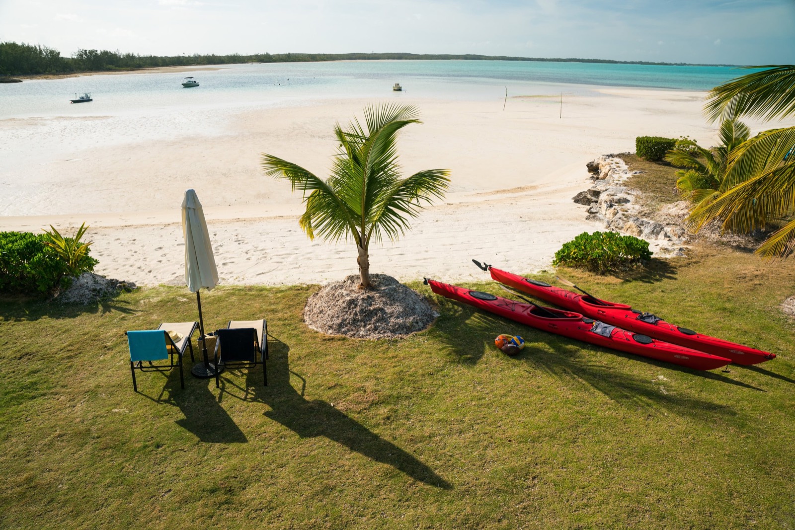 View over the lawn and kayaks onto a vast low-tide sand flat with boats anchored offshore