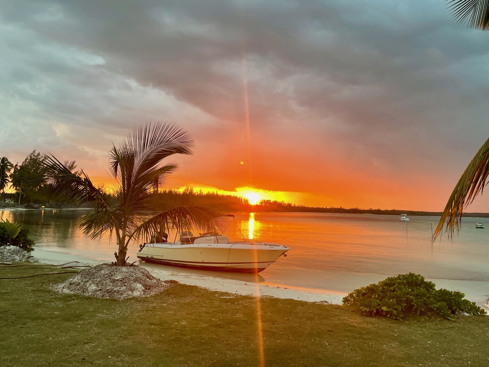 The cove at sunset: the boat pulled up on the sand under a palm, orange sky over glassy water