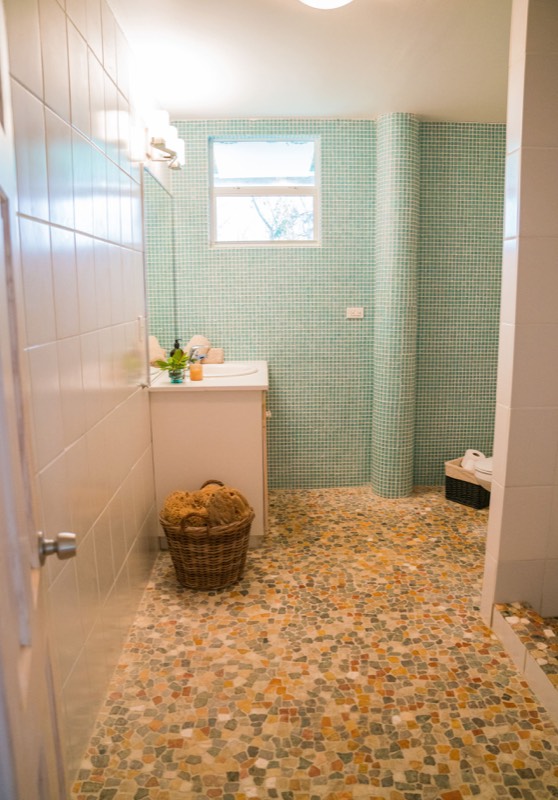 Bathroom with seafoam mosaic walls, curved walk-in shower and pebble floor