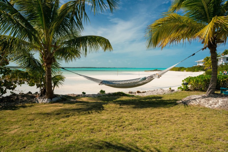 A rope hammock between two coconut palms, white sand and turquoise water behind
