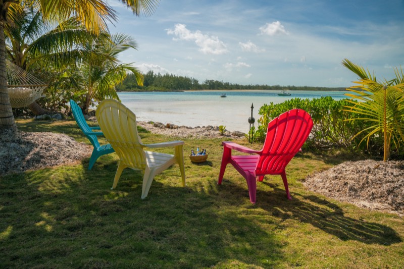 Three Adirondack chairs facing the calm bay, a bowl of cold Kalik beers between them