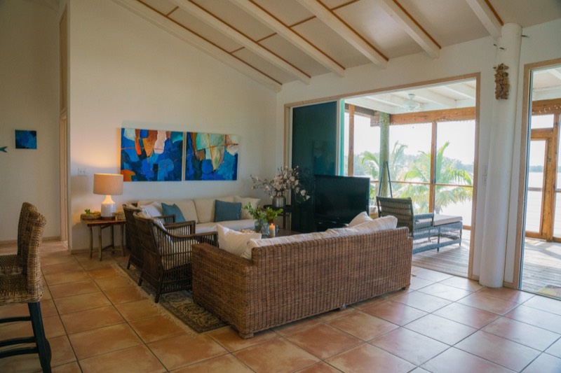 Living room with wicker seating, a blue triptych and vaulted beamed ceilings, open doors to the porch