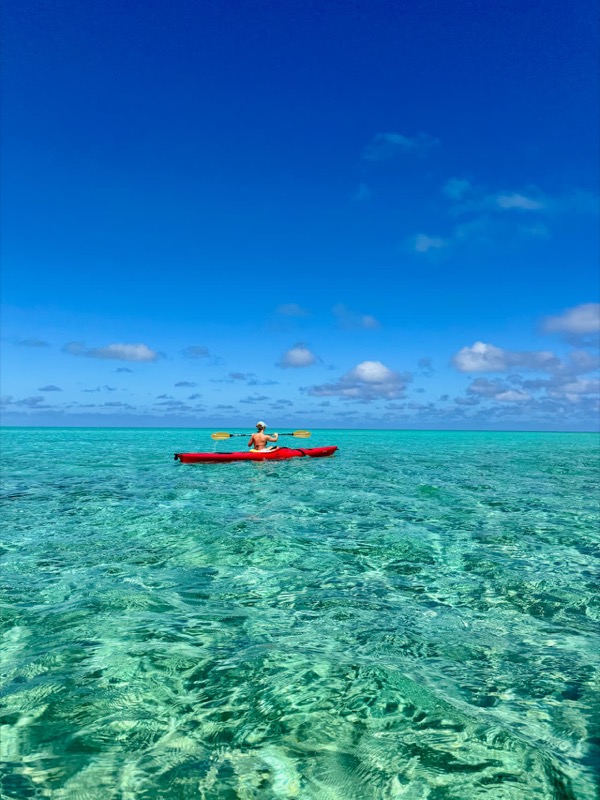A kayaker on gin-clear turquoise flats under a deep blue sky
