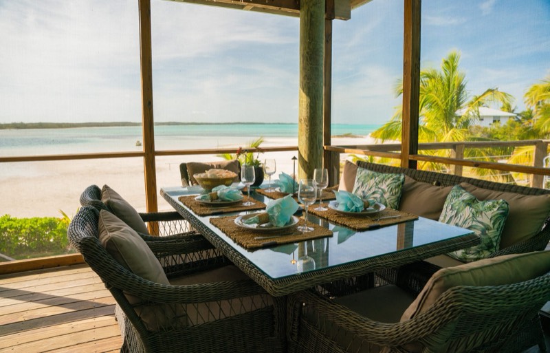 The screened veranda with wicker armchairs in warm afternoon light, beach and sea beyond
